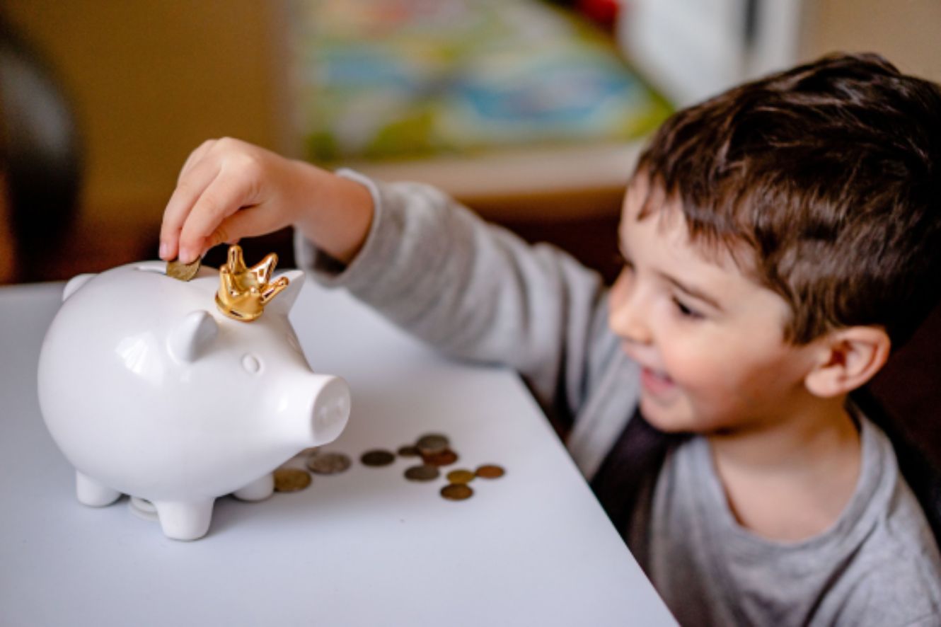 Small boy putting coins into a white ceramic piggy bank.